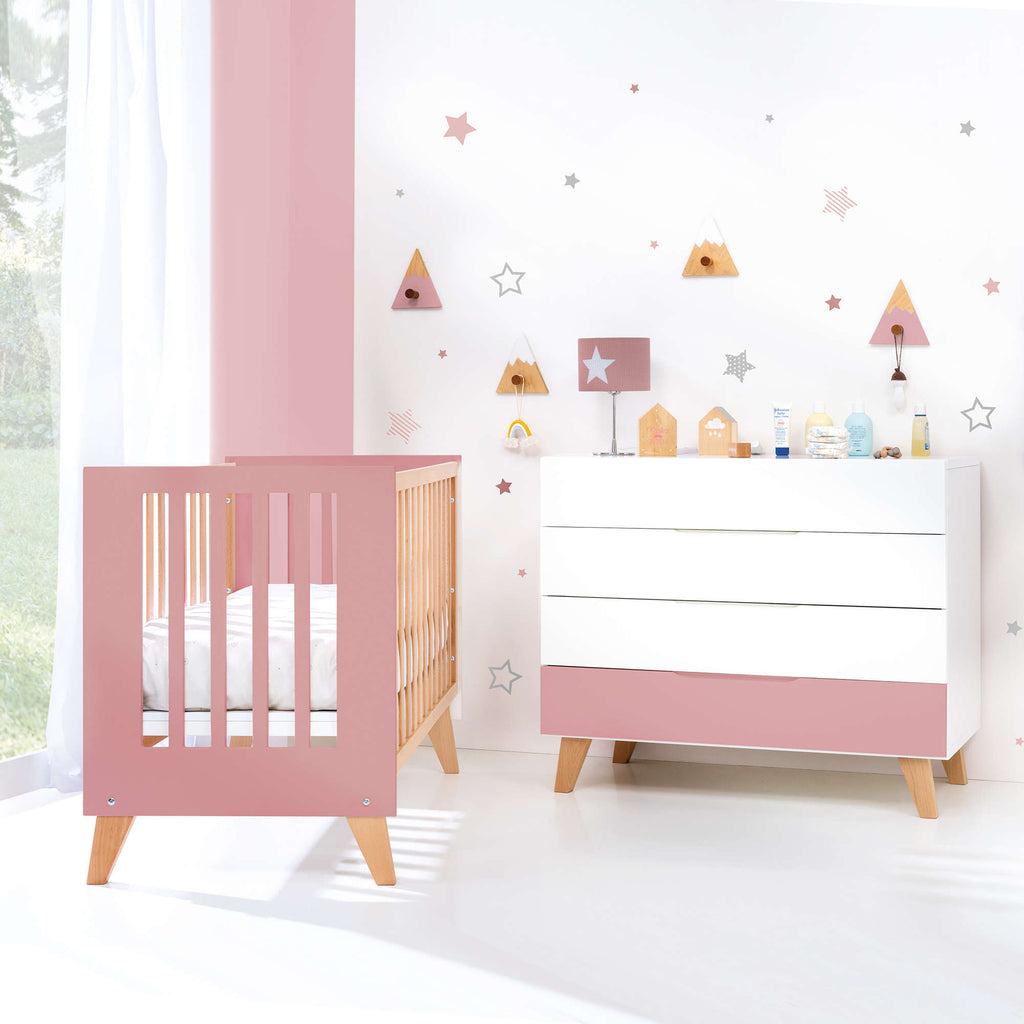 habitación de bebé de color blanco y rosa con cuna y cómoda